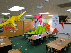 an empty classroom with desks and paper cranes hanging from the ceiling