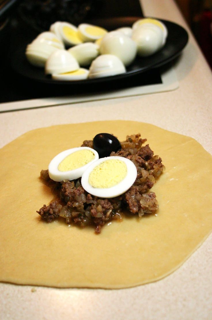 an uncooked tortilla with hard boiled eggs and meat in the center