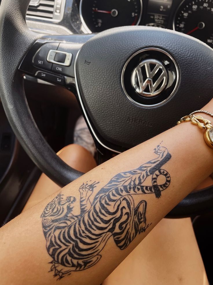 a woman's arm with a tiger tattoo on the inside of her car steering wheel