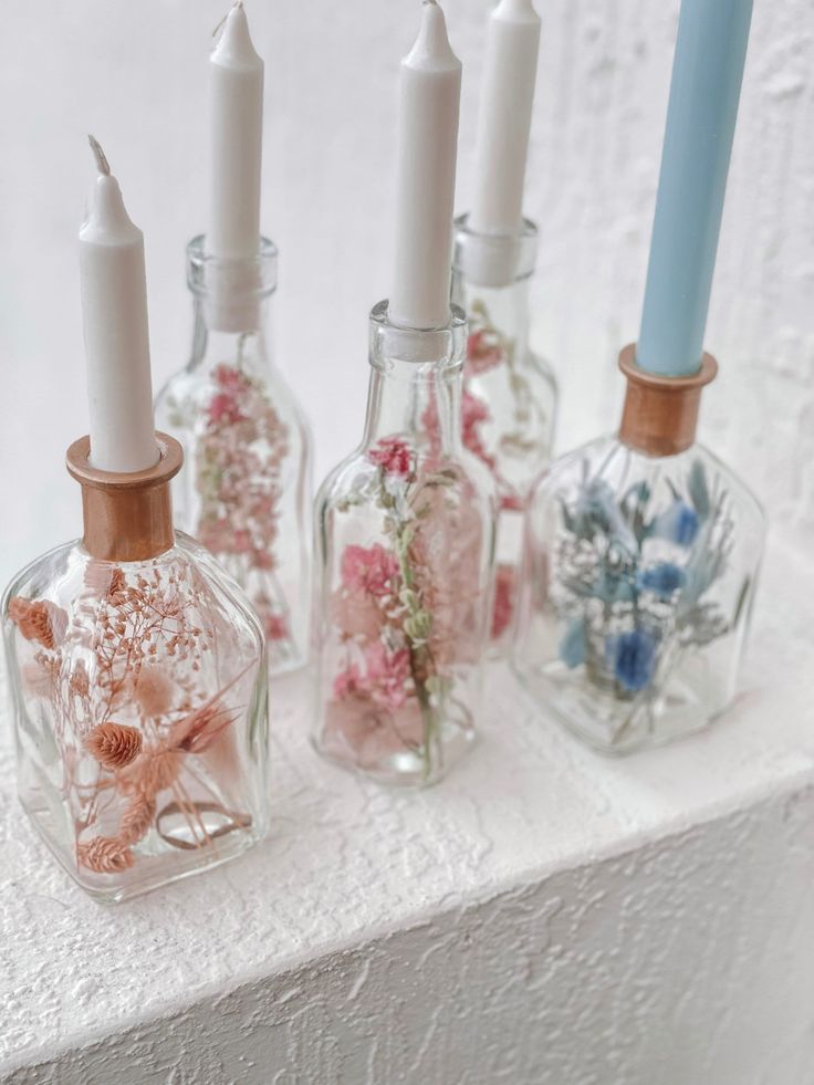 four glass bottles with flowers in them on a shelf