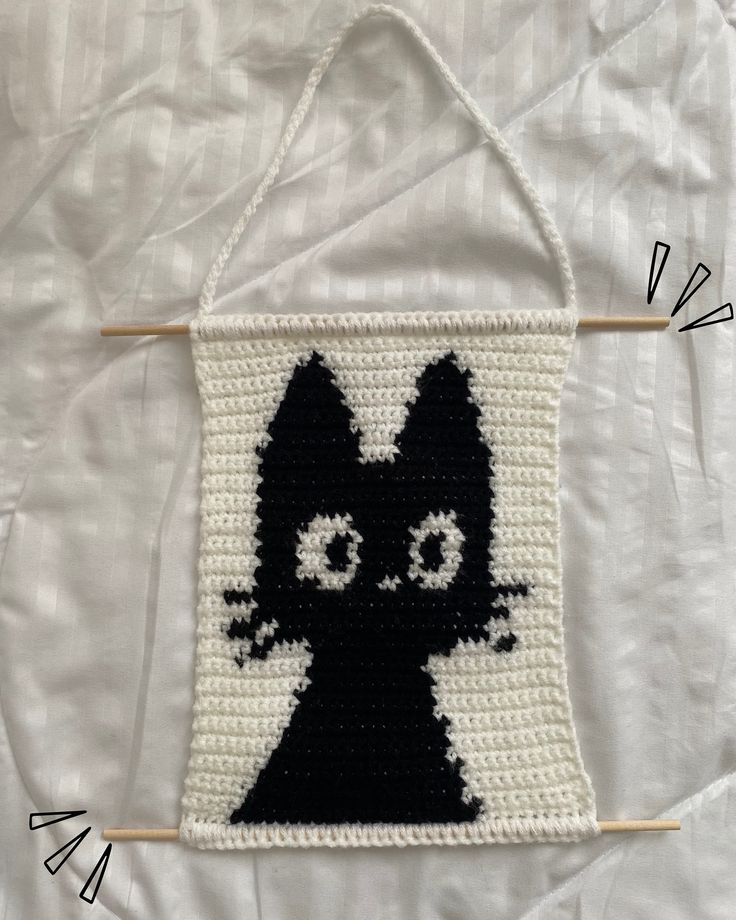 a crocheted black and white cat hanging on a wall