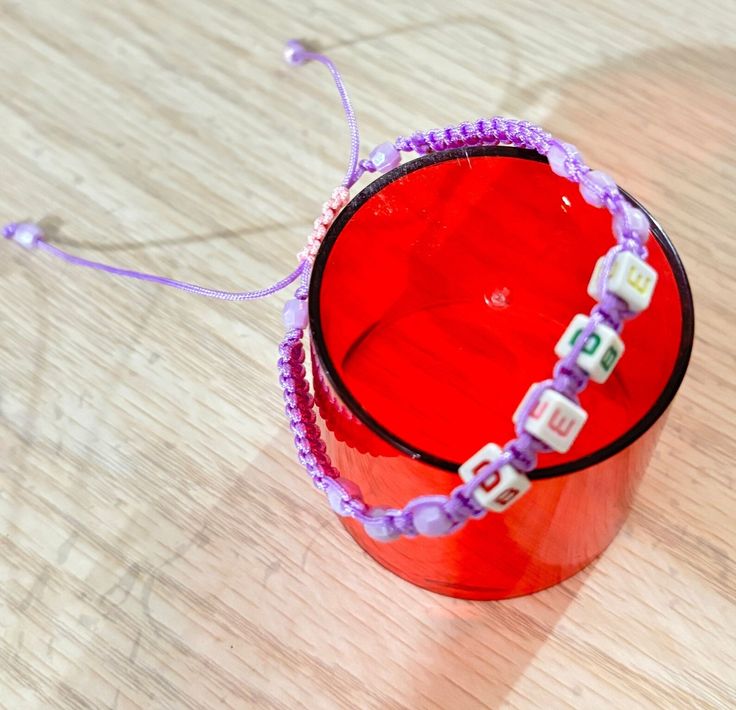 a red cup with beads on it sitting on top of a wooden table next to a string