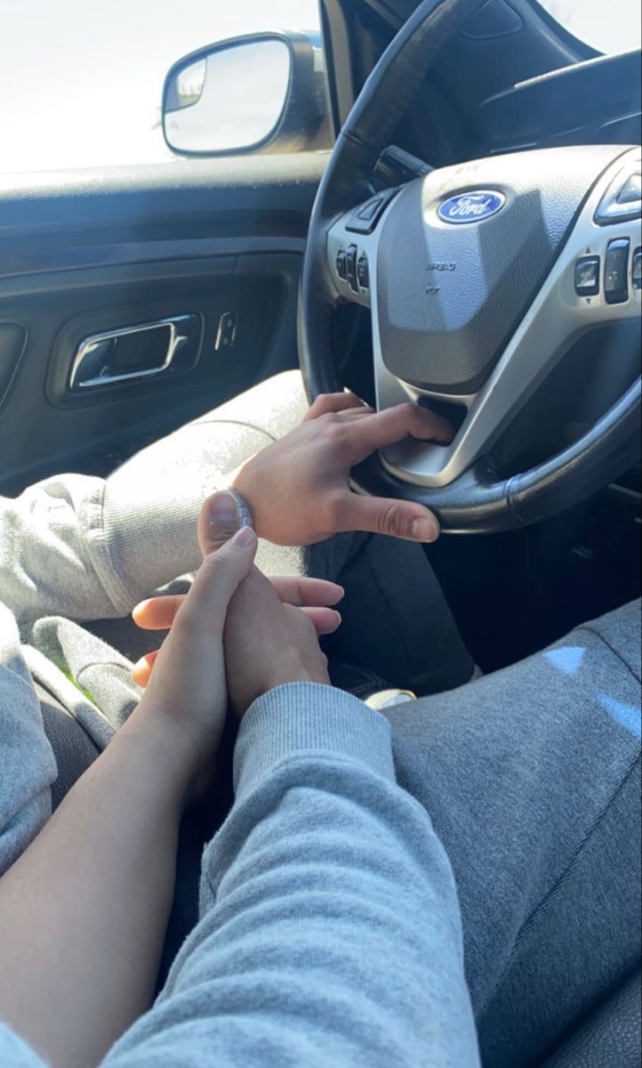 two people sitting in the driver's seat of a car with their hands on the steering wheel