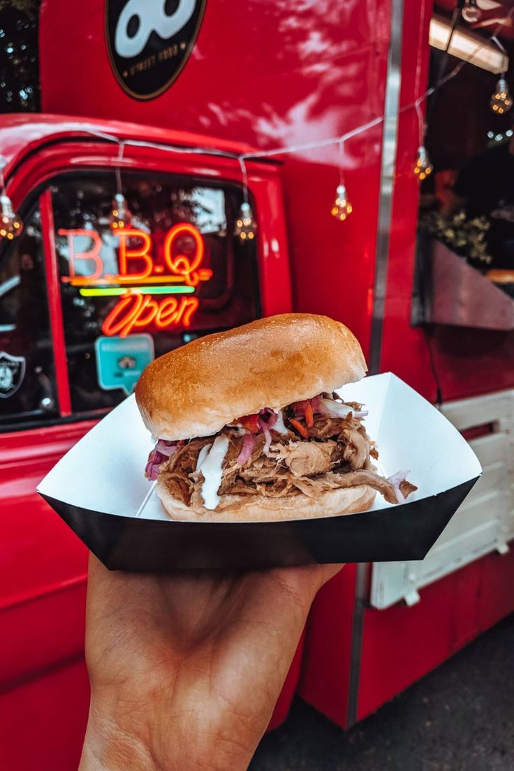 a person holding up a sandwich in front of a red truck with the door open