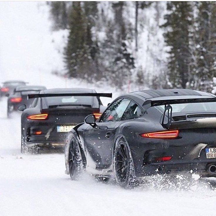 cars driving in the snow on a road with trees and snow covered ground behind them