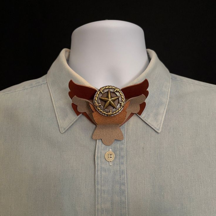 Wing Loops Neck Ties combine features of both a bow tie and a bolo tie. Its unique design is recognized by US Patent: 9,554664.  Made of Italian leathers and highlighted with a metal concho it offers a western appeal that fits with jeans and boots or combine with a tuxedo for a formal affair.  Dimensions: 3 1/2 inches wide x 3 inches tall x 1 inch thick Made with 2 layers of leather (Taupe and Whiskey) spiraled together and highlighted with a metal concho:  a center star with barbed wire border, Fits With Jeans, Bolo Country, Formal Jewelry, Western Star, Suit Men, Gold Highlights, Bolo Tie, Groom Suit, Tie Accessories