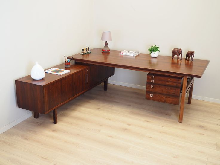 a wooden desk with two drawers and a vase on top, in front of a white wall