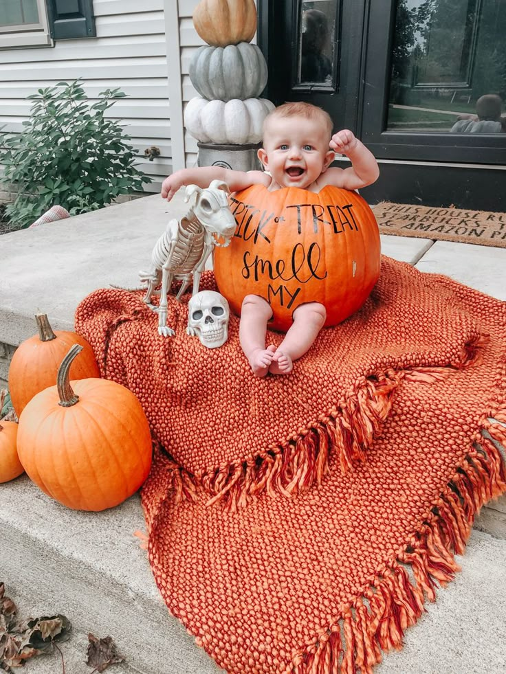 a baby sitting on top of a pumpkin in front of a house with the words trick or treat written on it