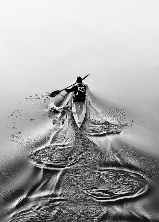 black and white photograph of a person in a canoe paddling on the water with two oars