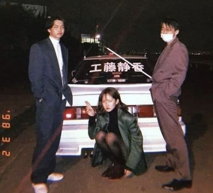 two men and a woman standing next to a car