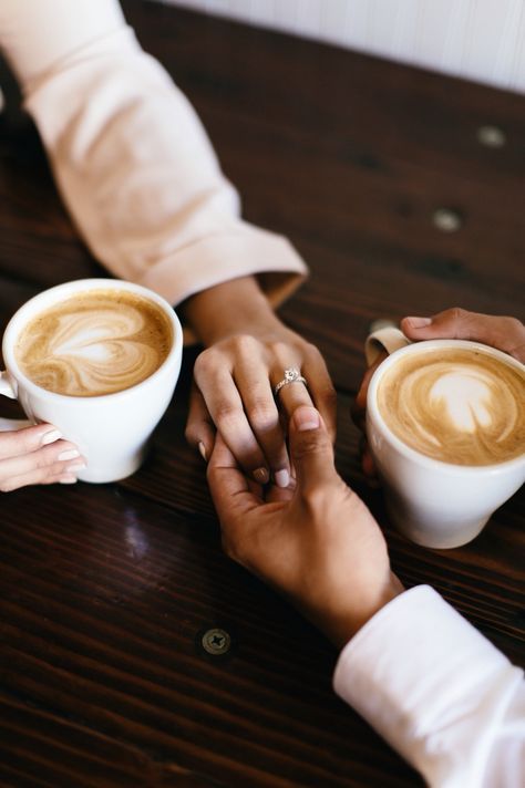 two people holding hands while sitting at a table with cups of coffee in front of them