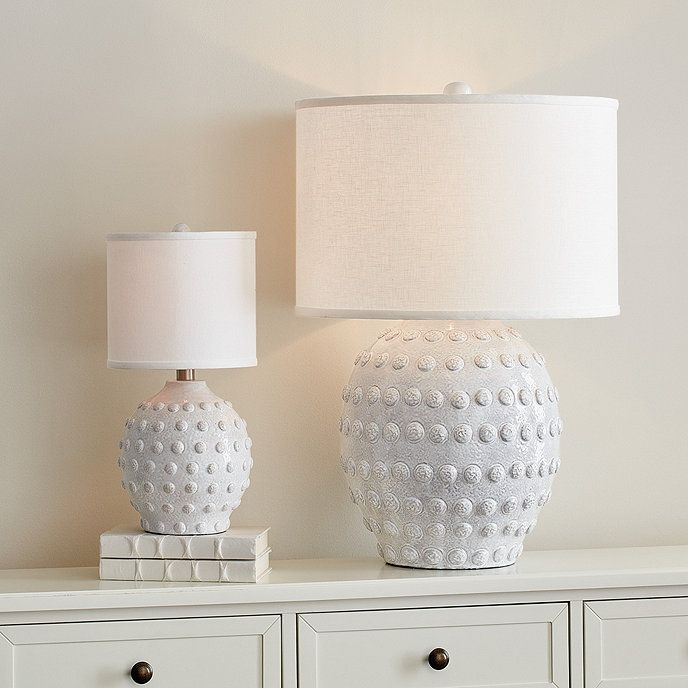 two white vases sitting on top of a dresser next to a lamp with a white shade