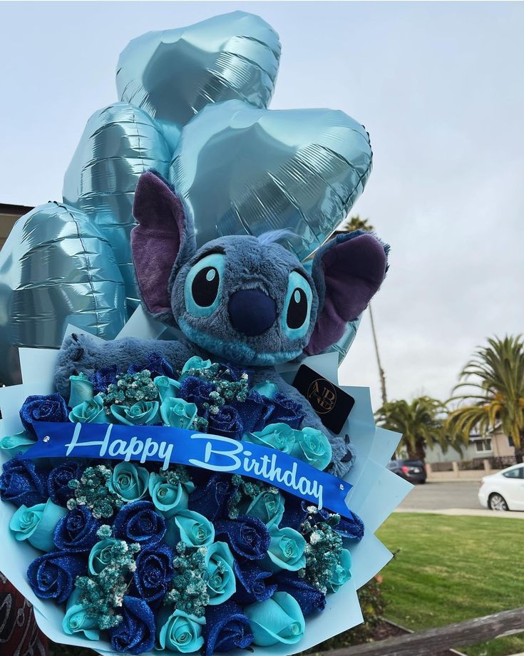 a bouquet of flowers with a stuffed animal in the center and balloons behind it that say happy birthday