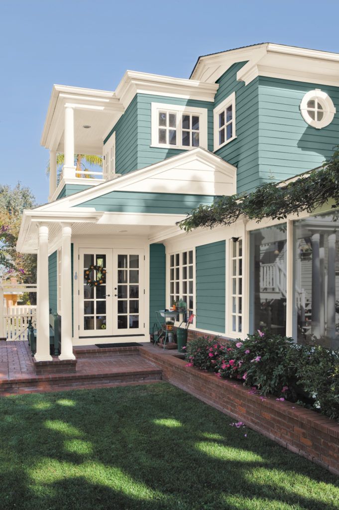 a blue house with white trim on the front and side windows, grass in front