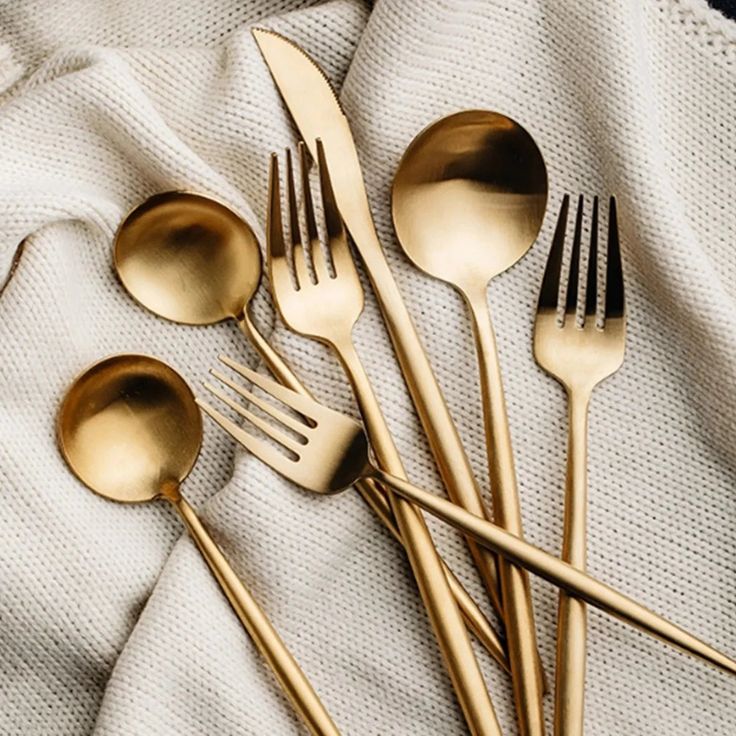 gold colored forks and spoons on a white cloth