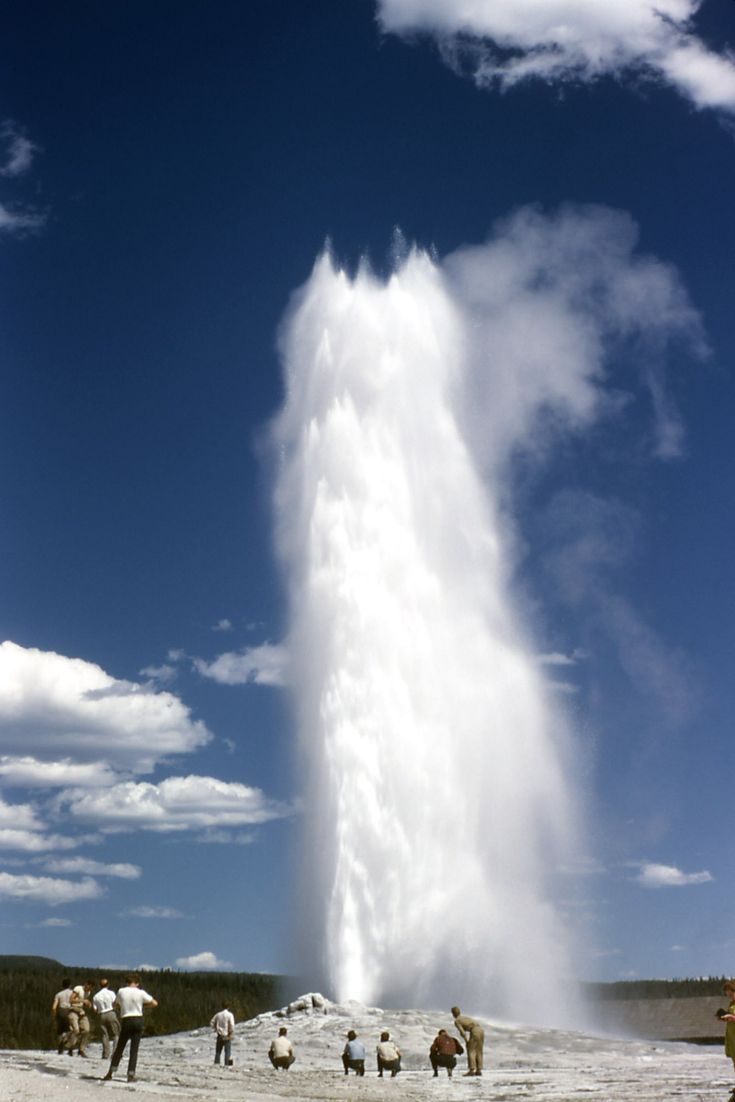 people are standing in front of a geyser spewing water into the sky