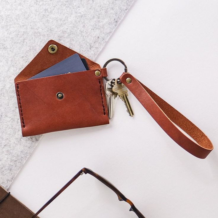 a leather wallet with two keys hanging out of it's front pocket, next to a pair of glasses