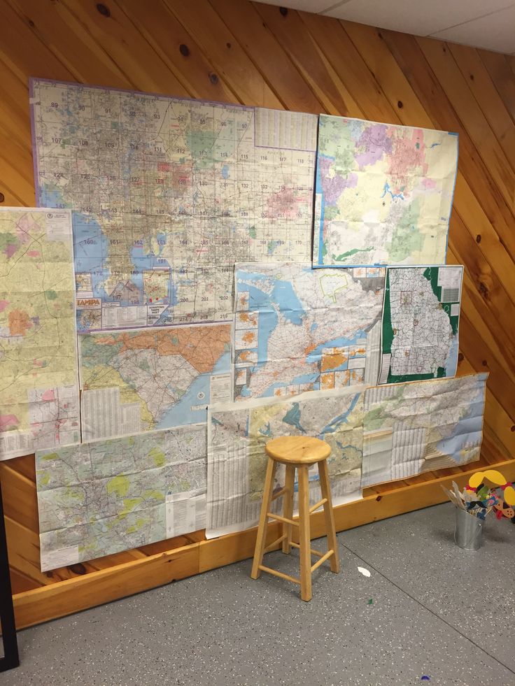 a wall covered in maps and stools next to a wooden table with flowers on it