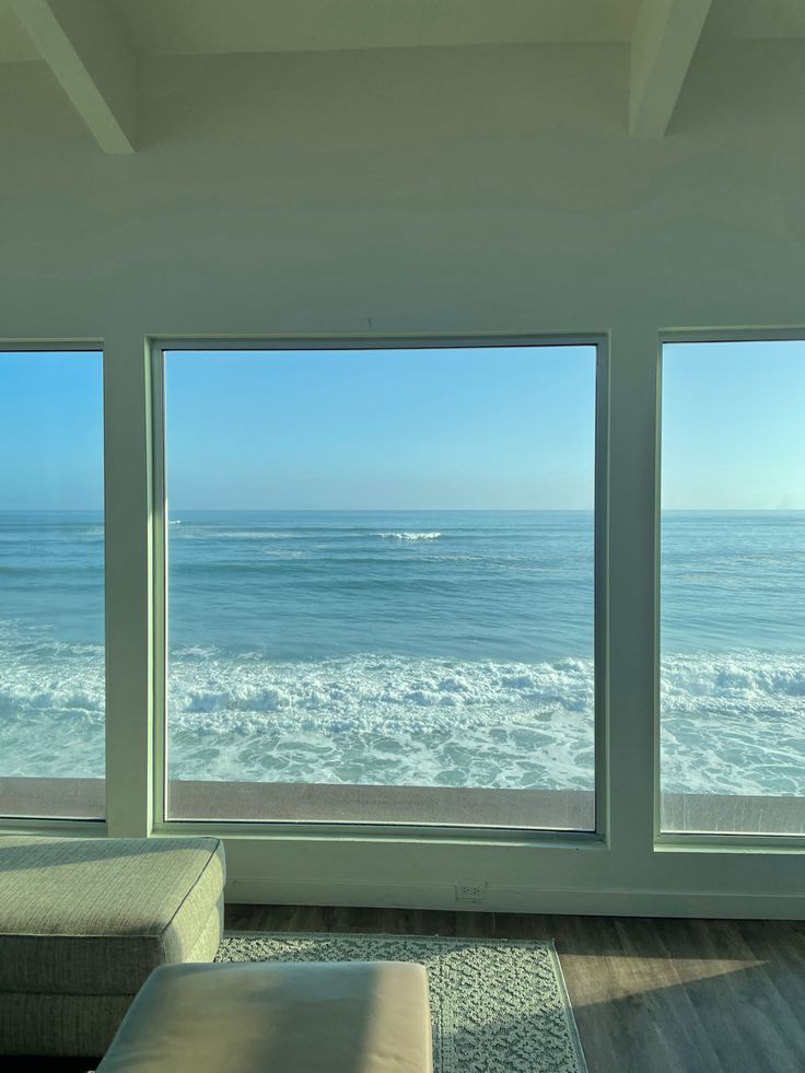 a living room filled with furniture and large windows looking out to the ocean on a sunny day