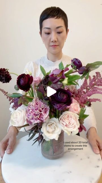 a woman holding a vase filled with flowers on top of a table