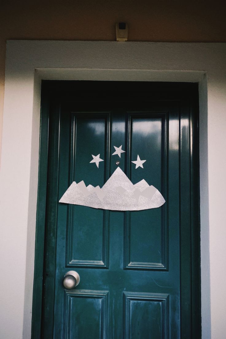 a green door with white stars painted on the front and side of it, above which is a mountain