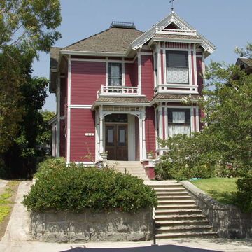 a red house with white trim on the front and stairs leading up to it's second story