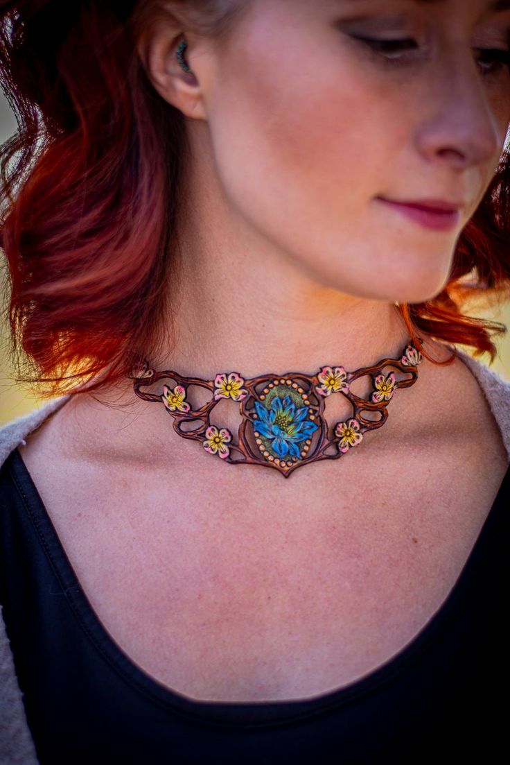 Elevate your accessory game with our exclusive hand-carved leather chokers, a marriage of craftsmanship and elegance. Inspired by the enchanting charm of faeries and the rustic essence of cottagecore aesthetics, each choker showcases a symphony of delicate branches, intertwining vines, and intricate floral touches.At the heart of this masterpiece is a meticulously hand-carved blue lotus flower, symbolizing purity, beauty, and grace. The deep nuances of the leather, combined with the soft glow of Bohemian Brown Flower Jewelry, Fantasy Festival Choker Jewelry, Handmade Fantasy Choker For Festivals, Handmade Fantasy Choker For Gifts, Handmade Fantasy Choker As Gift, Handmade Fantasy Festival Choker, Whimsical Adjustable Choker, Adjustable Whimsical Choker, Handmade Whimsical Choker Jewelry