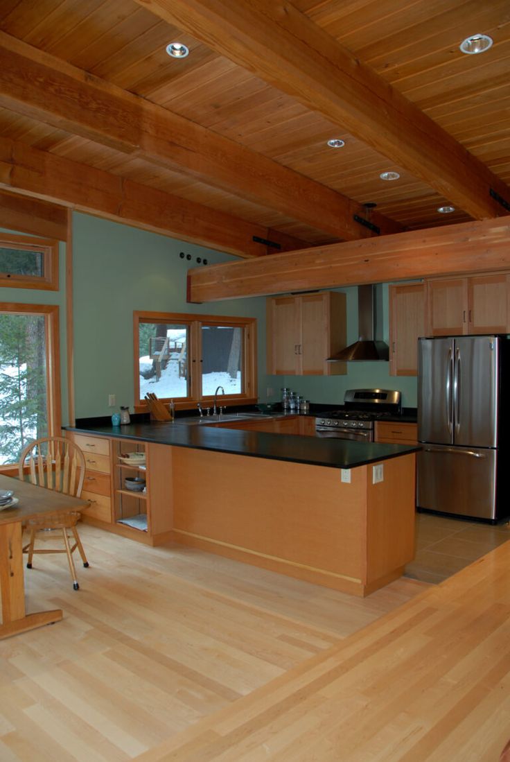 a kitchen with wood floors and wooden ceilinging next to a dining room table in front of an open window