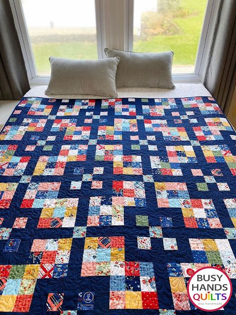 a bed with a blue quilt on top of it next to two pillows and a window