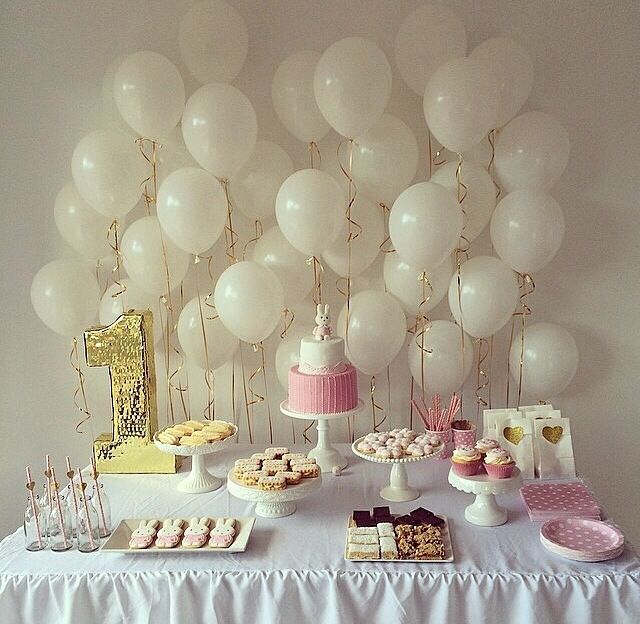 a table topped with lots of white balloons and desserts next to a cake on a plate