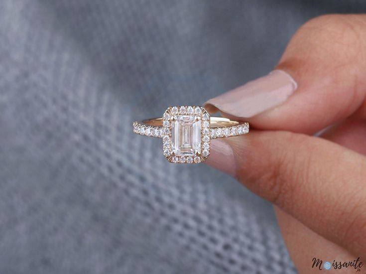 a woman's hand holding a ring with an emerald stone and diamonds on it