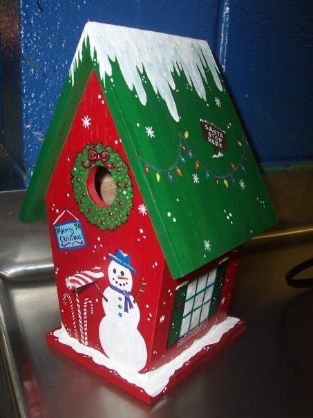 a red birdhouse with a green roof and snowman on it's side