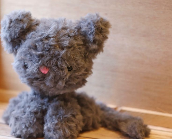 a small gray teddy bear sitting on top of a wooden floor next to a wall