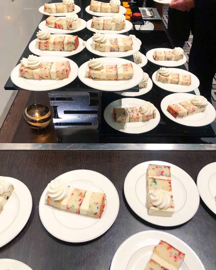 desserts are arranged on white plates in front of a black counter with people standing around