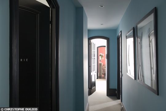 an empty hallway with blue walls and pictures on the wall, along with black doors