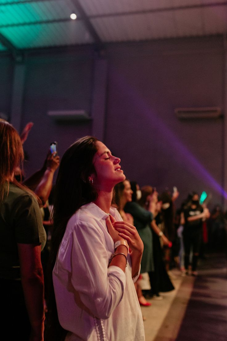 a woman standing in front of a crowd holding her hands together and looking up at the sky