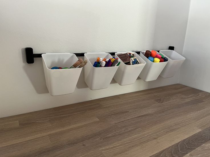 three white bins with pencils and crayons in them on a wall