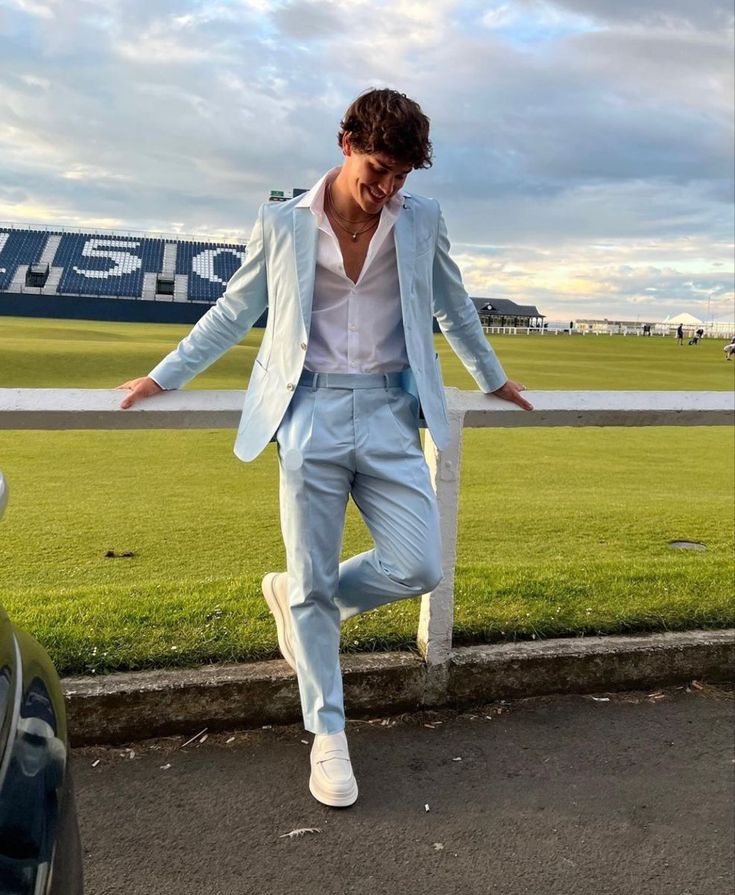 a man in a blue suit and white shirt is walking on the sidewalk near a field