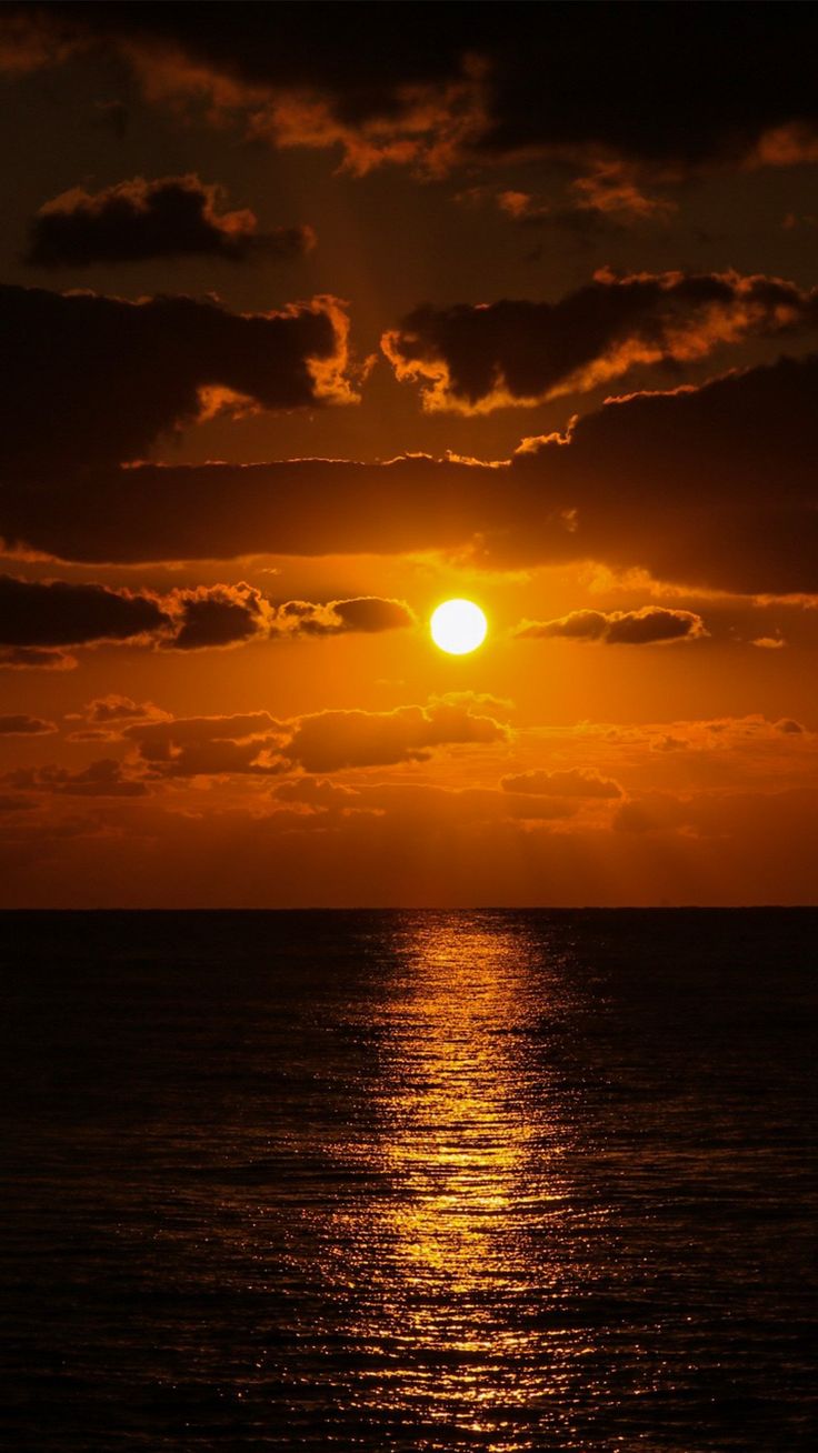 the sun is setting over the ocean with clouds in the sky and reflecting on the water