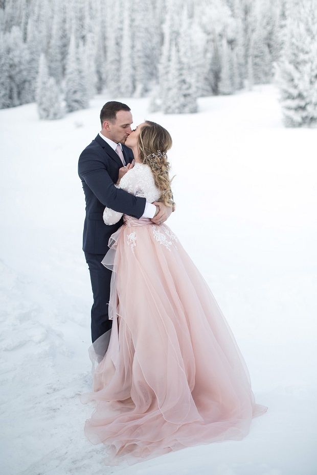 a bride and groom kissing in the snow with pine trees in the backgroud