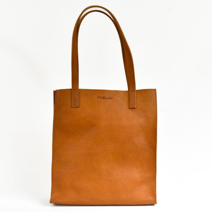 Tall market tote crafted in pebbled vegetable tanned leather and an unlined interior. The sleek minimal design makes it a great everyday bag for work, school or a visit to the farmers market. It features reinforced bottom support and large interior pocket to keep your keys and phone close by. - Pebbled Full Grain Italian Vegetable-Tanned leather - Unlined Interior - Includes 1 large interior pocket - Reinforced bottom support - Ethically Handcrafted in the Dominican Republic Modern Everyday Shoulder Bag In Vegetable Tanned Leather, Everyday Vegetable Tanned Leather Bag With Double Handle, Everyday Cognac Shoulder Bag With Smooth Grain, Everyday Cognac Bag With Leather Lining, Everyday Double Handle Vegetable Tanned Leather Bag, Everyday Cognac Textured Leather Bag, Classic Everyday Shoulder Bag In Vegetable Tanned Leather, Minimalist Shoulder Bag With Leather Lining For Daily Use, Classic Vegetable Tanned Leather Shoulder Bag For Everyday