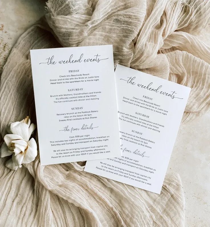 two wedding program cards on top of a bed with a flower in the middle and an unbuttoned sheet behind them