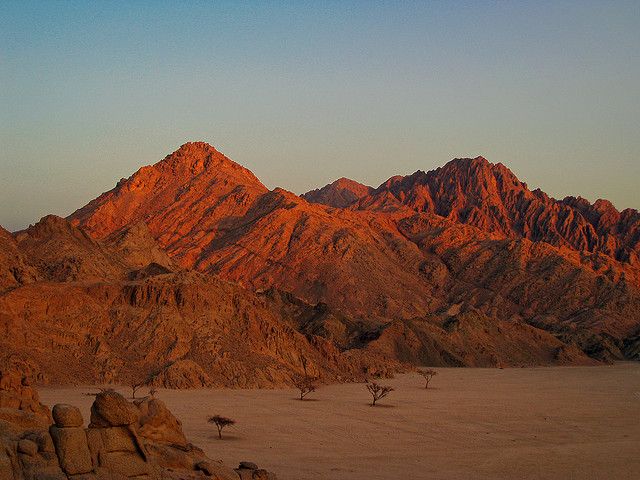 the sun is setting on some mountains in the desert with sparse grass and rocks around them