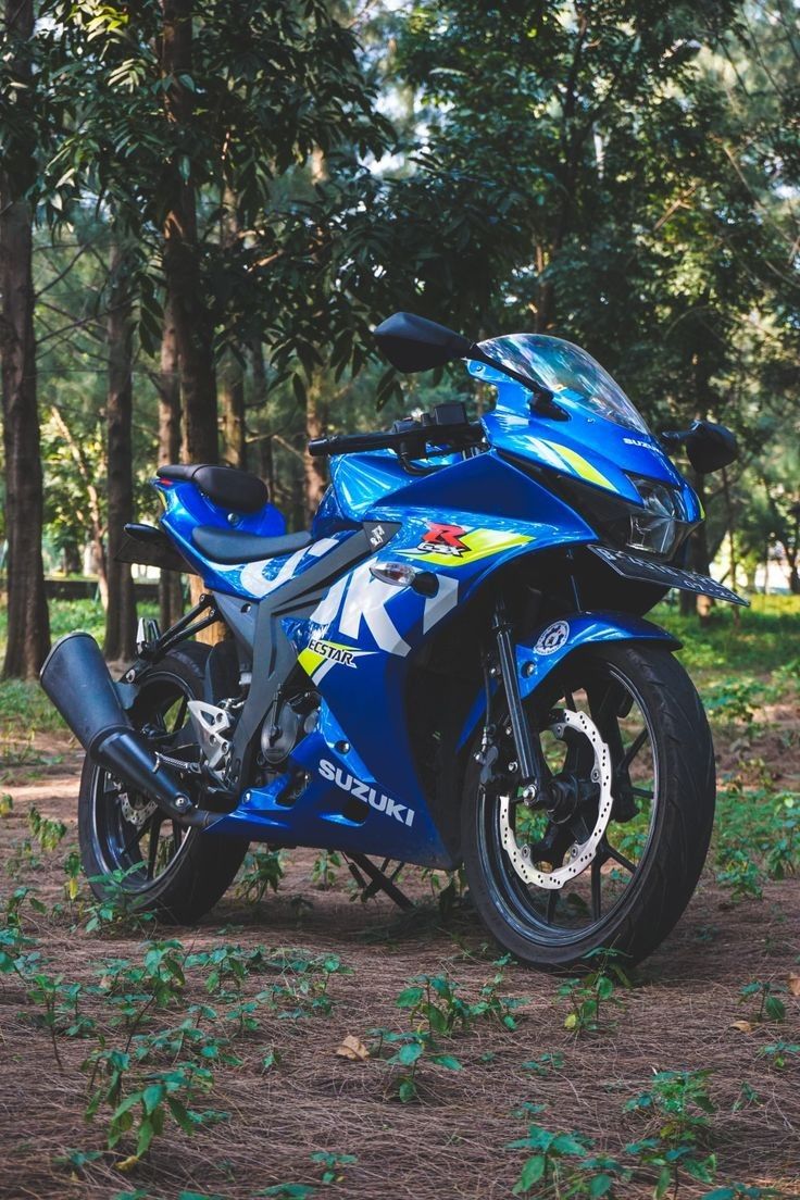 a blue motorcycle parked on top of a dirt road next to some green trees and bushes