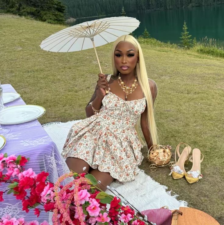 a woman sitting on top of a grass covered field holding an umbrella over her head