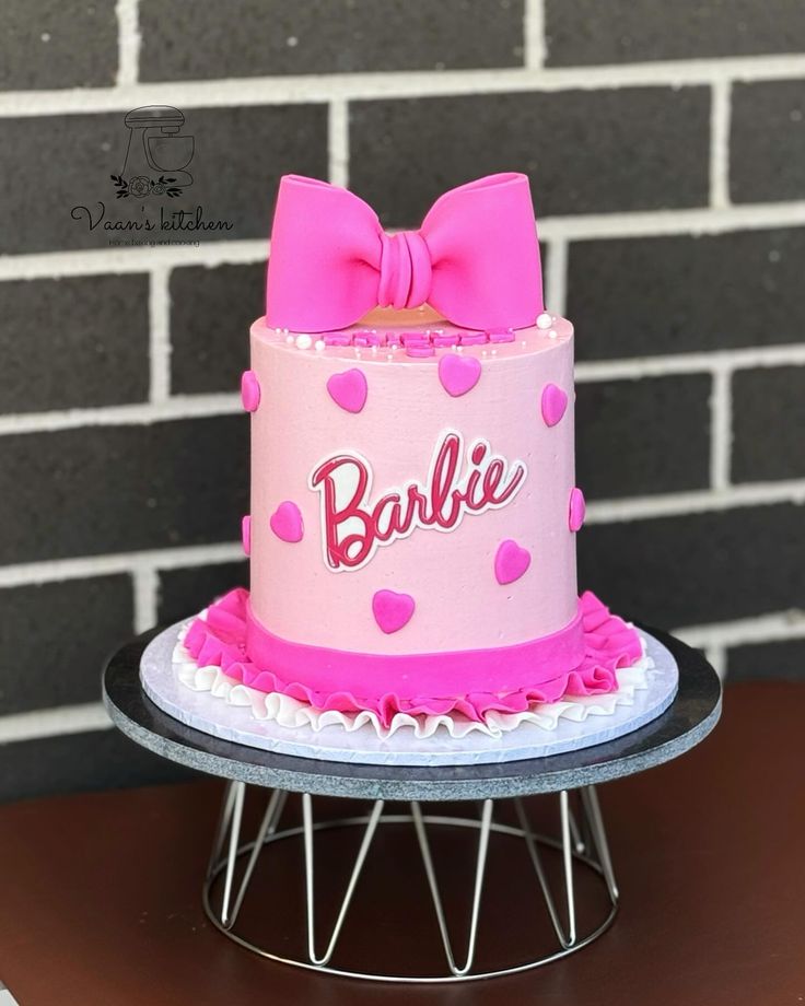 a pink cake with a bow on top sitting on a table next to a brick wall