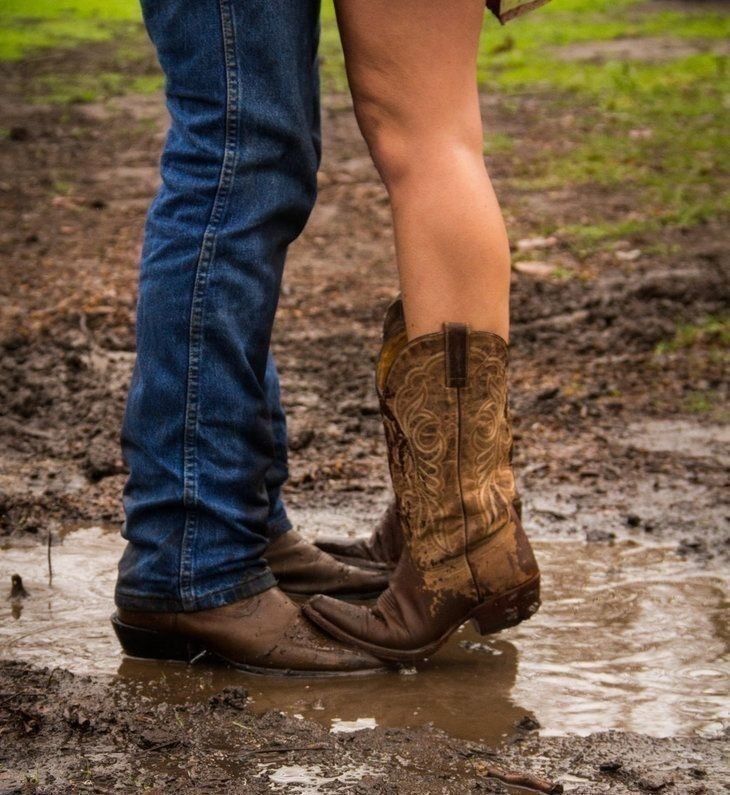 a man and woman standing in the mud with cowboy boots on their feet, holding each other's legs