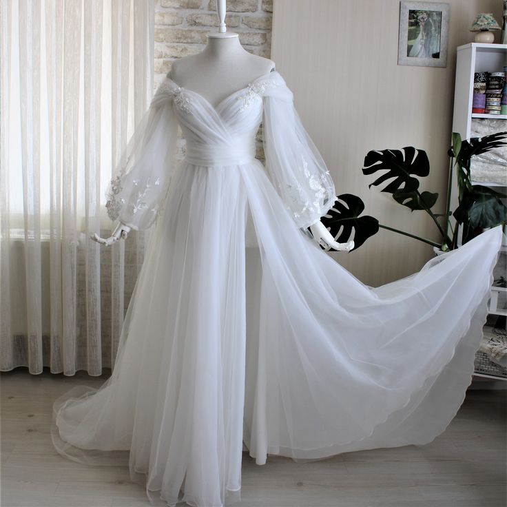 a white wedding dress on display in front of a brick wall with curtains behind it