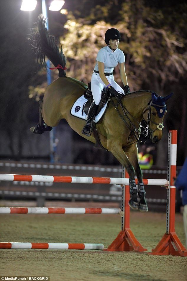 a woman riding on the back of a brown horse jumping over an orange obstacle course