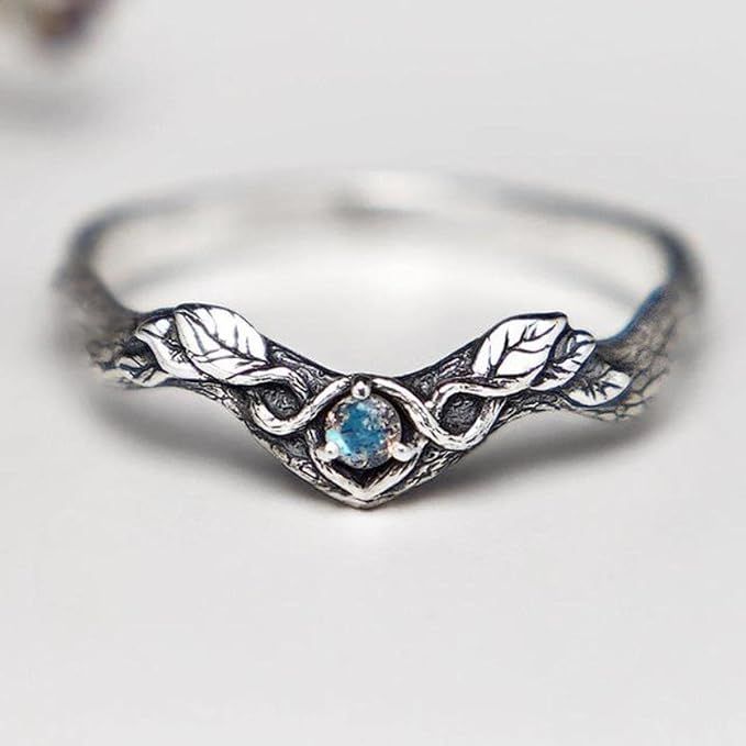 a silver ring with leaves on it and a blue stone in the middle, sitting on a white surface